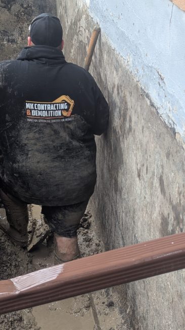 mk labourer in an exterior basement waterproofing trench digging a whole to connect to the new sump pump pit to prepare for instalation